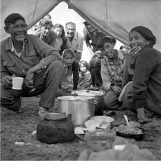 Image of people in a tent gathered around cooking pots
