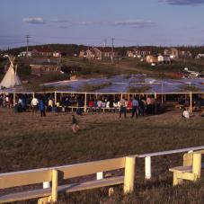 Every summer, the Dene of all communities participate in a national assembly, such as this one in Fort Good Hope (Rádeyı̨lı̨kóé) in 1980. An elaborate public address system allows participants to speak and hear proceedings in English, Tłı̨chǫ, North Slavey, South Slavey, Chipewyan and Gwich'in.
